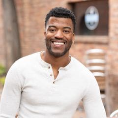 Lorne Jenkins, Executive Director of Mini Money, smiling in a white henley in front of a brick wall.