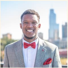 Davian Rhodes of Neurofin, Technology, in a light checked jacket and red bow tie with a city skyline behind him.